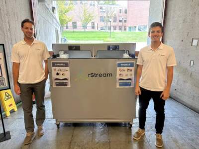 Ethan Walko, left, and Ian Goodine, right, with the machine they designed to photograph trash at UMass Amherst as part of a larger project to build a machine that can sort garbage from recycling. (Alden Bourne/NEPM)