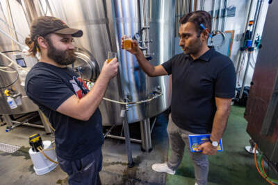 Dorchester Brewing head brewer Andy Johnson and Rupee Beer founder Van Sharma raise glasses as they sample some of the new IPA being brewed at the Dorchester Brewing Company. (Jesse Costa/WBUR)