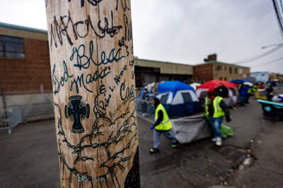 Two volunteers from the Newmarket Business Improvement District remove a tent from Atkinson Street as they pass a telephone pole with the words, “God bless Mass and Cass” inscribed on it. (Jesse Costa/WBUR)