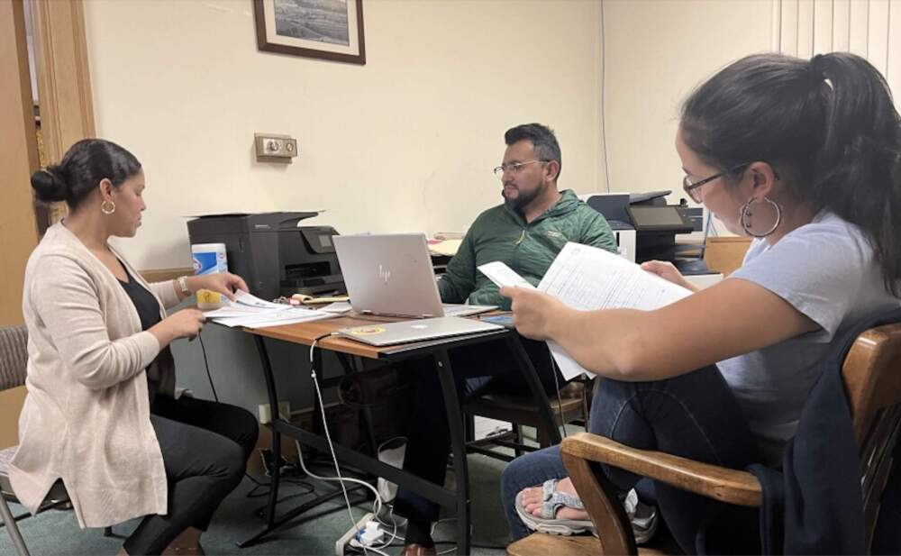Community organizers Emily Rodriguez (left), Leninn Torres (center) and Sarah Takasaki (right) parse through documents from the Registry of Motor Vehicles at the Pioneer Valley Project in Springfield, Massachusetts. (Nirvani Williams/NEPM)