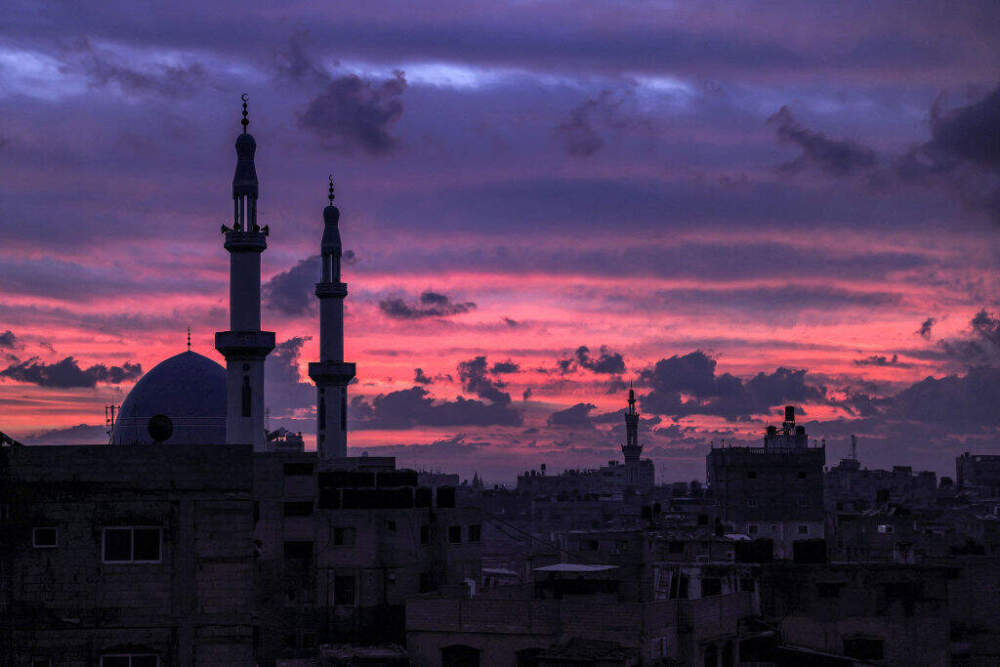 The sky is illuminated red at sunset behind mosque minarets in Rafah in the southern Gaza Strip near the border with Egypt on December 17, 2023 amid continuing battles between Israel and the militant group Hamas. (Photo by SAID KHATIB/AFP via Getty Images)