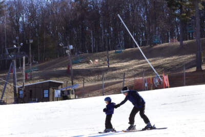 A child learns to ski on the beginners slope, adjacent to snowless snowboarding park, at rear, at the Ski Bradford ski area, Tuesday, Feb. 14, 2023, in in Bradford, Mass. (Charles Krupa/AP)