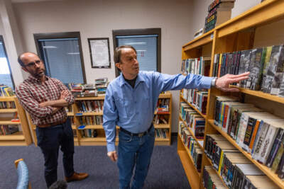 Inmate John Sheehan points out, with the help of Brian Stokes, how the books have now been organized by the author’s name which makes it easier to find the titles he wants. (Jesse Costa/WBUR)