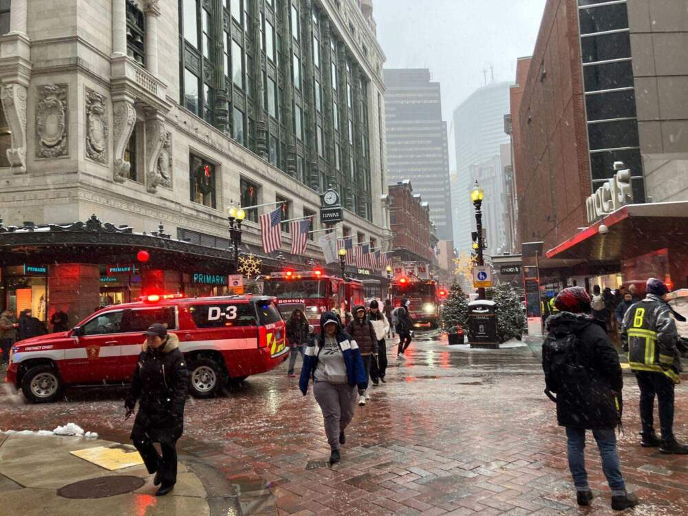 Pedestrians walk by fire trucks stationed outside of the Downtown Crossing station as snow falls. (SHNS)
