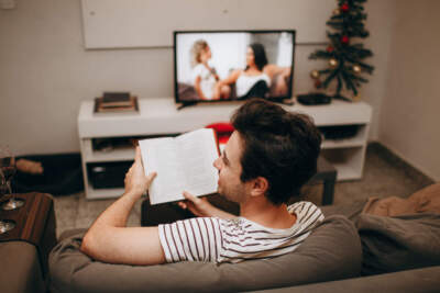 A man reads a book in front of the TV. (Helena Lopes/Getty Images)