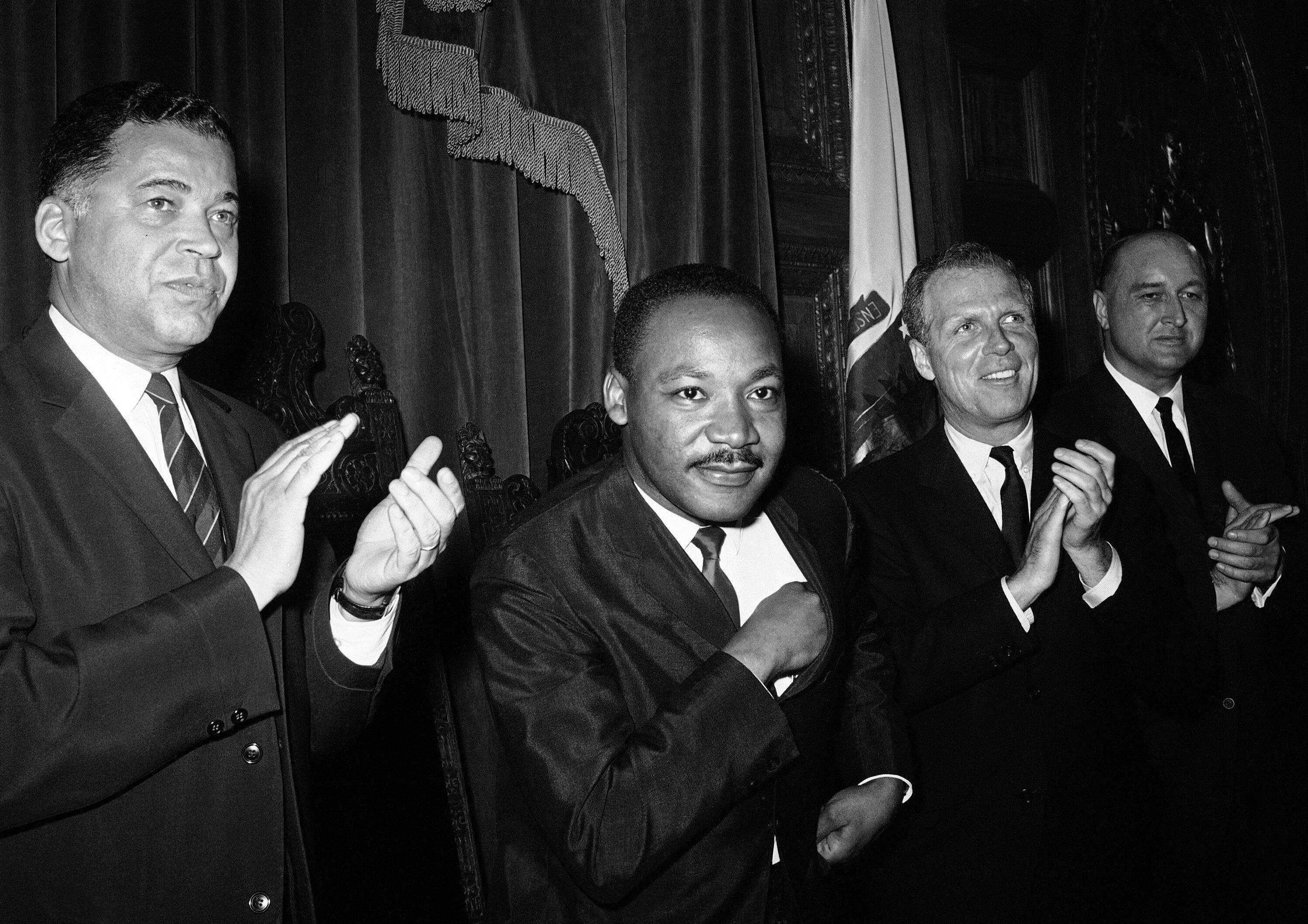 Dr. Martin Luther King Jr., as he sits down following his speech to the joint session of the Massachusetts Legislature in Boston, April 22, 1965. Applauding at left is Massachusetts Attorney Gen. Edward W. Brooke. King will lead a civil rights march to Boston Common. Others are unidentified. (AP Photo)