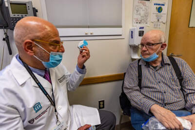 Dr. Miguel Divo shows his patient, Dr. Joel Rubinstein, a dry powder inhaler. It has a much lower carbon footprint than a traditional inhaler while being equally effective for many patients with asthma.  (Jesse Costa/WBUR)