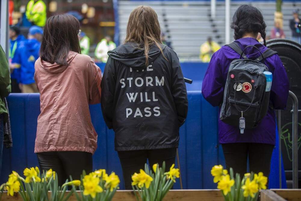 A woman with a jacket that read, “The Storm Will Pass,” watches things happening on the marathon course. (Jesse Costa/WBUR)