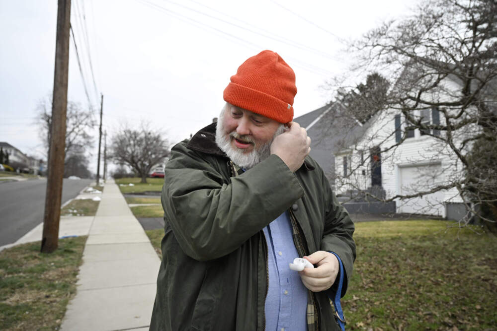 Casey Rosseau places earbuds in his ears to listen to an e-book while he walks with his dog in West Hartford, Conn. (Jessica Hill/AP)