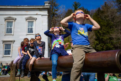 Kids sitting on a cannon in front of the Vermont State House watch the total eclipse begin in Montpelier, Vermont on April 8, 2024. (Jesse Costa/WBUR)