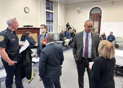 Newton Police Chief John Carmichael Jr. (left) and Suffolk County District Attorney Kevin Hayden (right) talk with Governor's Council members before a hearing on Gov. Maura Healey's mass cannabis possession pardon. (Sam Doran/SHNS)