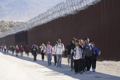 A group of people, including many from China, walk along the wall after crossing the border with Mexico to seek asylum, Tuesday, Oct. 24, 2023, near Jacumba, Calif. A major influx of Chinese migration to the United States on a relatively new and perilous route through Panama's Darién Gap jungle has become increasingly popular thanks to social media. (Gregory Bull/AP)