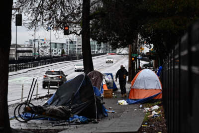 A pedestrian walks past an encampment of tents after crossing Hoyt Street in Portland, Oregon on Jan. 24, 2024. (Patrick T. Fallon/AFP via Getty Images)