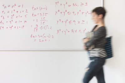 A young woman walks in front of a whiteboard with math problems. (Getty)
