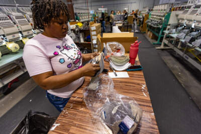 Musette Jean-Pierre, an immigrant from Haiti, inspects a hat on the factory floor of the New Bedford-based company Ahead. As she awaits her immigration hearing, she was granted authorization to work. (Jesse Costa/WBUR)