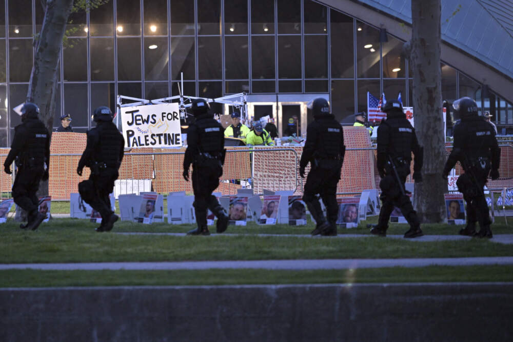 A line of police in riot gear walk past police dismantling pro-Palestinian encampment at MIT, before dawn Friday in Cambridge. (Josh Reynolds/AP)